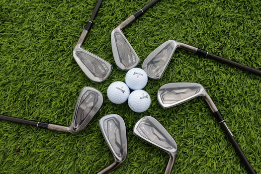 Arrangement of golf clubs and balls on a lush green grass surface, captured from above.