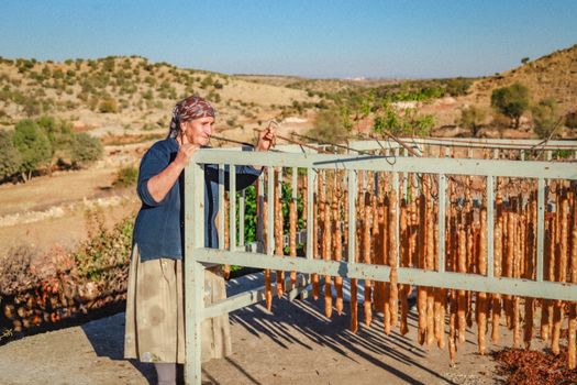 A woman tends to traditional dried fruit strings in rural Midyat, Türkiye.