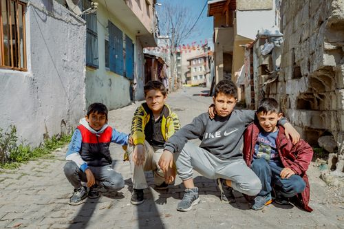 Free Four boys squatting in a sunny street in Tekirdağ, Türkiye. Stock Photo
