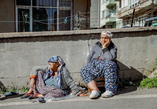 Two elderly women sit along a sunlit street in Tekirdağ, Türkiye, enjoying a peaceful moment.