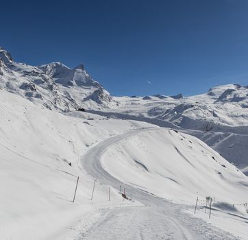 Stunning winter view of snow-covered Alps under a clear blue sky, depicting a peaceful mountain scene.