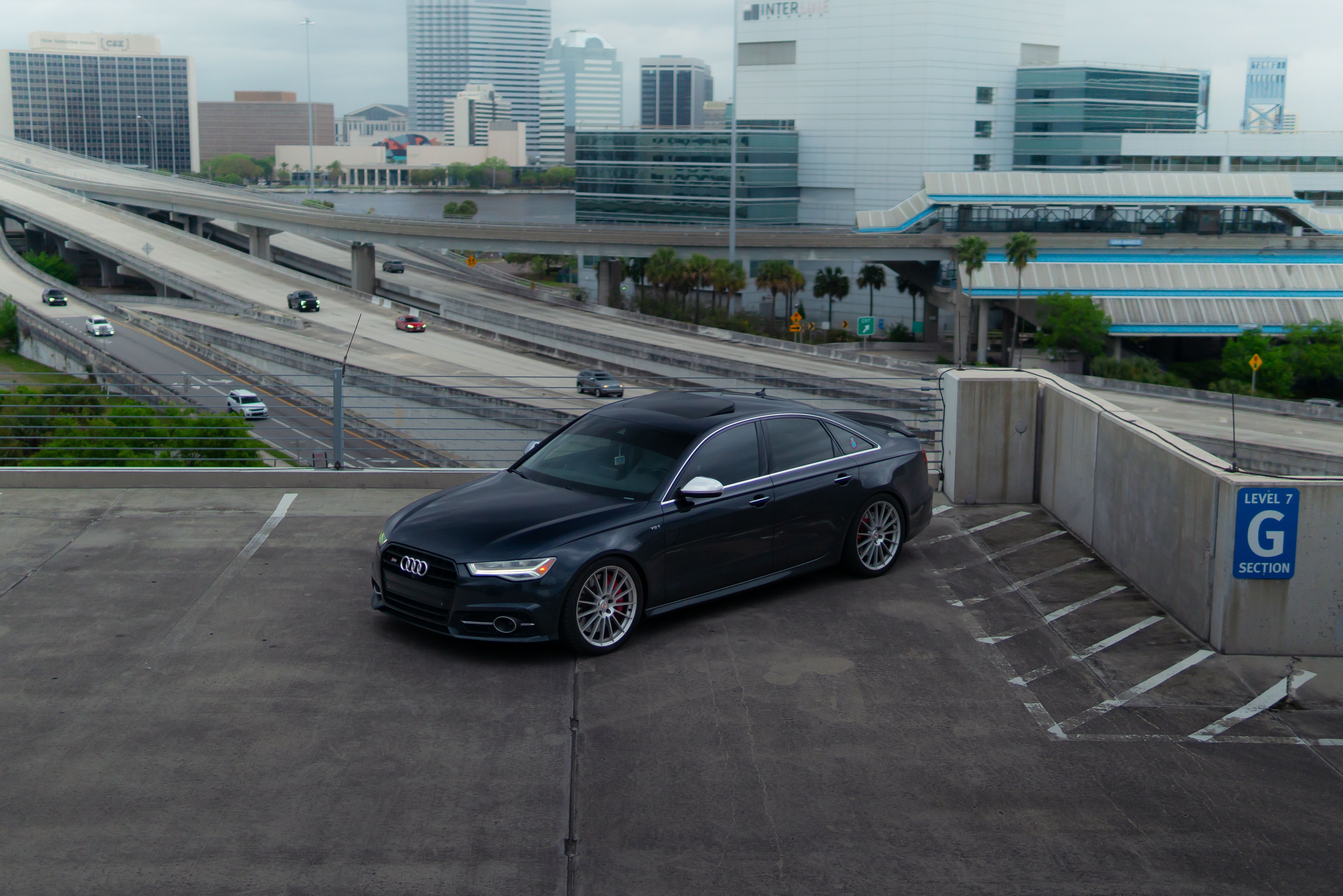 A sleek black sports car parked on a rooftop with a city skyline in the background.