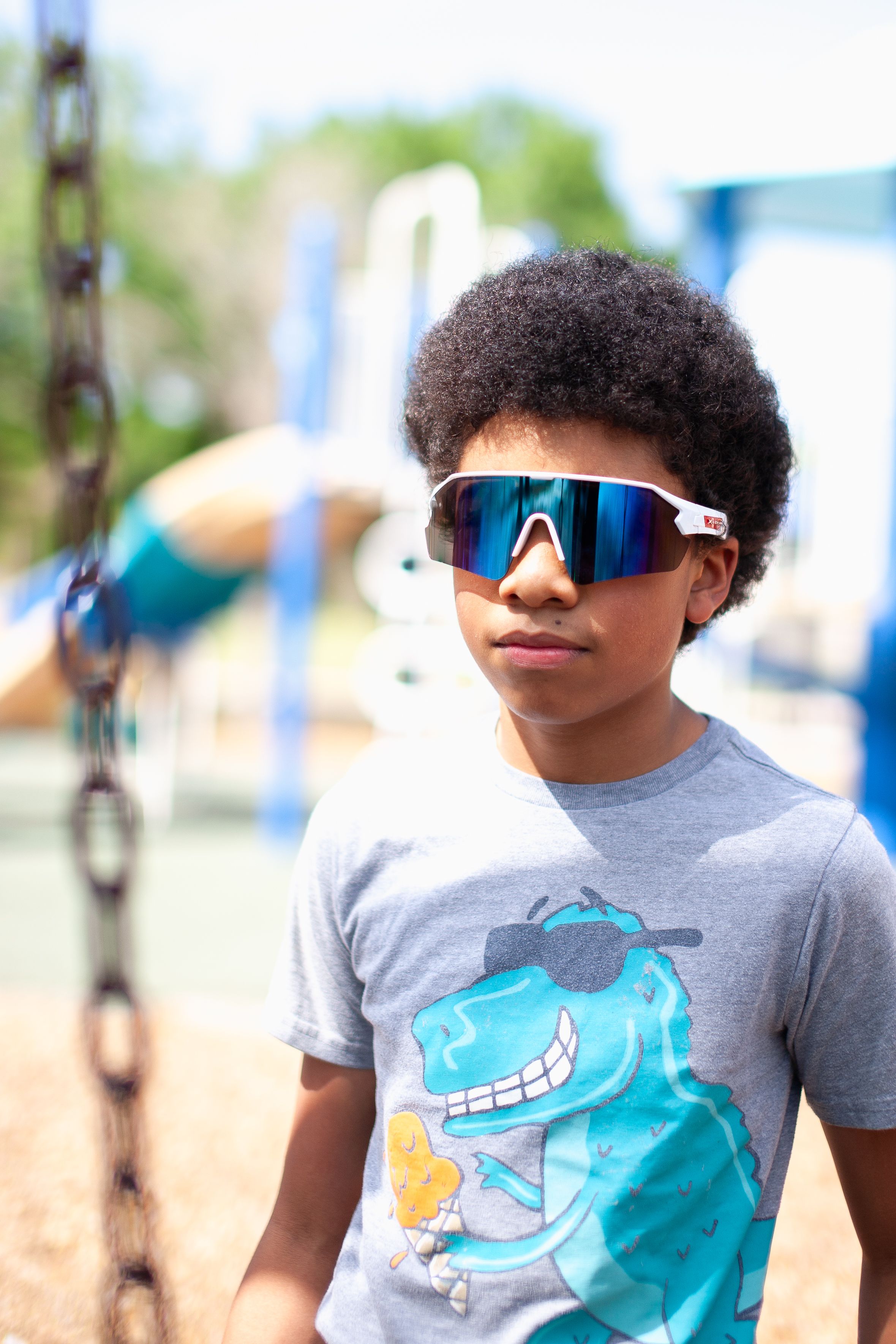 Fashionable young boy with sunglasses poses outdoors at a Miami playground.