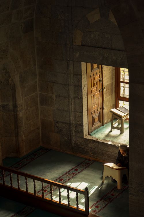 Free A person reading in a calm, sunlit mosque interior with intricate architecture. Stock Photo