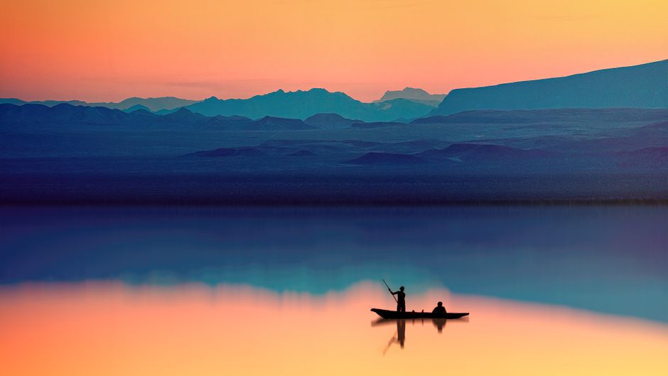 Silhouette of fishermen on a boat at sunset with mountains in the background.