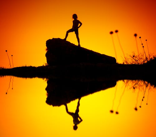 бесплатная Силуэт ребенка, стоящего на скале Стоковое фото