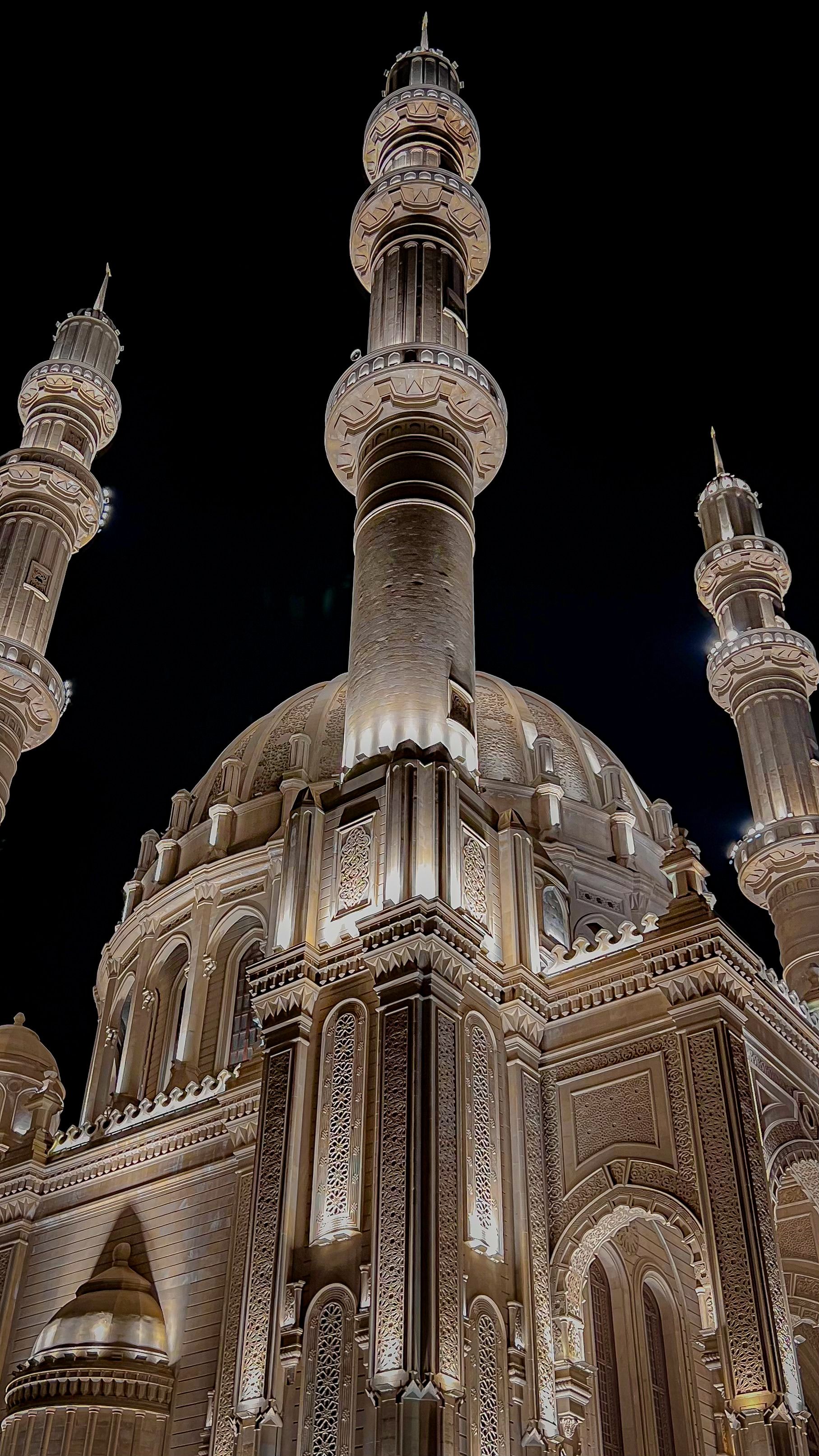 Majestic view of a mosque with ornate minarets and detailed architecture, beautifully lit at night.