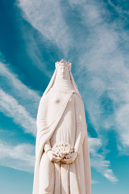 Striking statue of Virgin Mary with crown and flowers under vibrant blue sky, exuding serenity and grace.