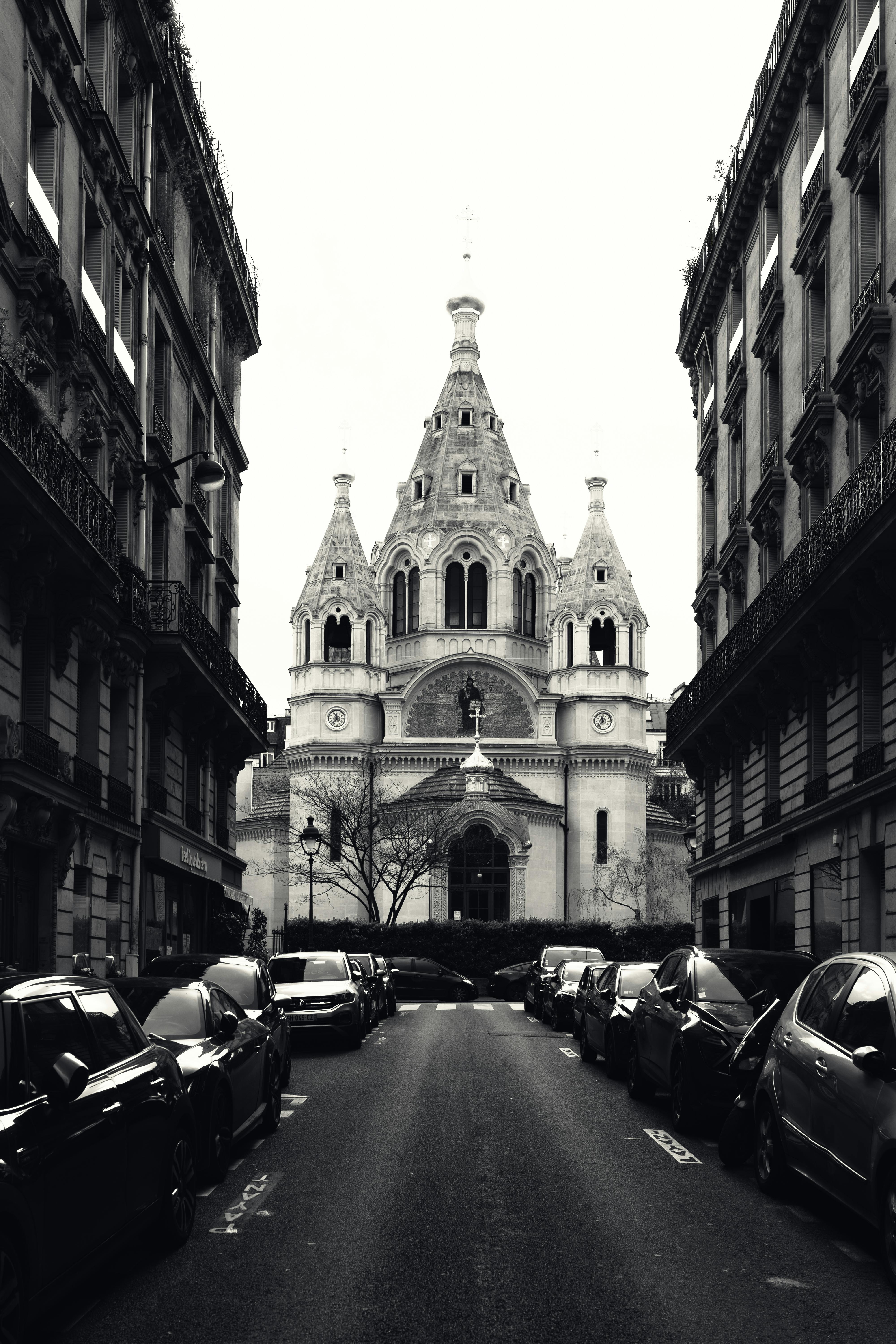Black and white image of a historic Paris church framed by urban streets and parked cars.