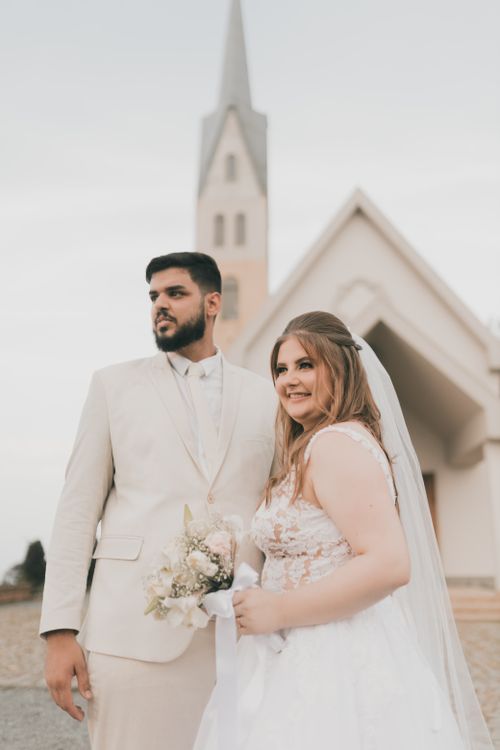 Free Elegant wedding couple posing in front of a church, capturing a special romantic moment. Stock Photo