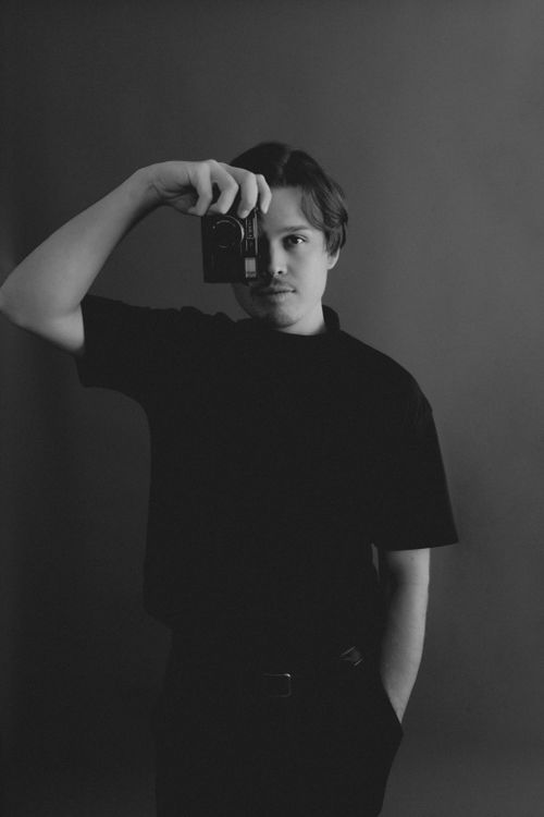 Free Artistic black and white portrait of a young man holding a camera in a studio setting. Stock Photo