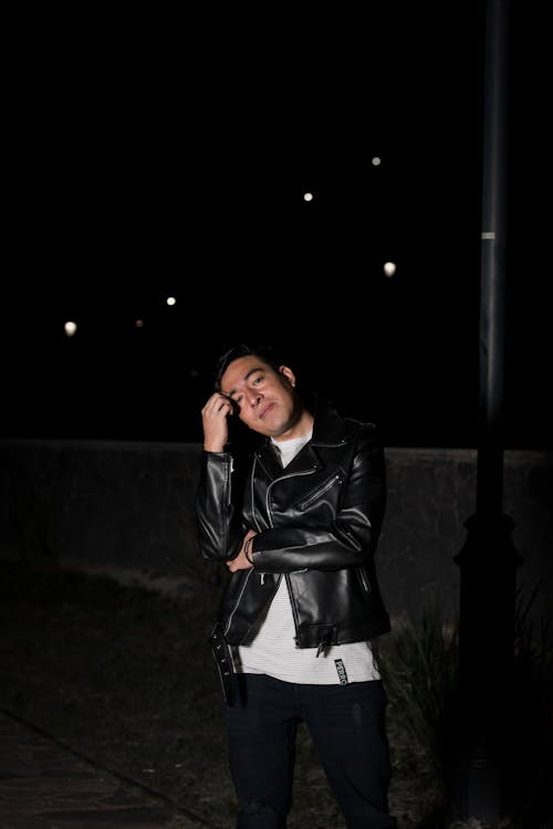 A Man in a Leather Jacket Standing Outside at Night 