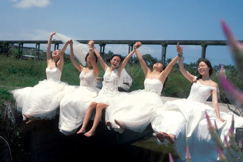 Women in White Dresses Sitting with Raised Hands