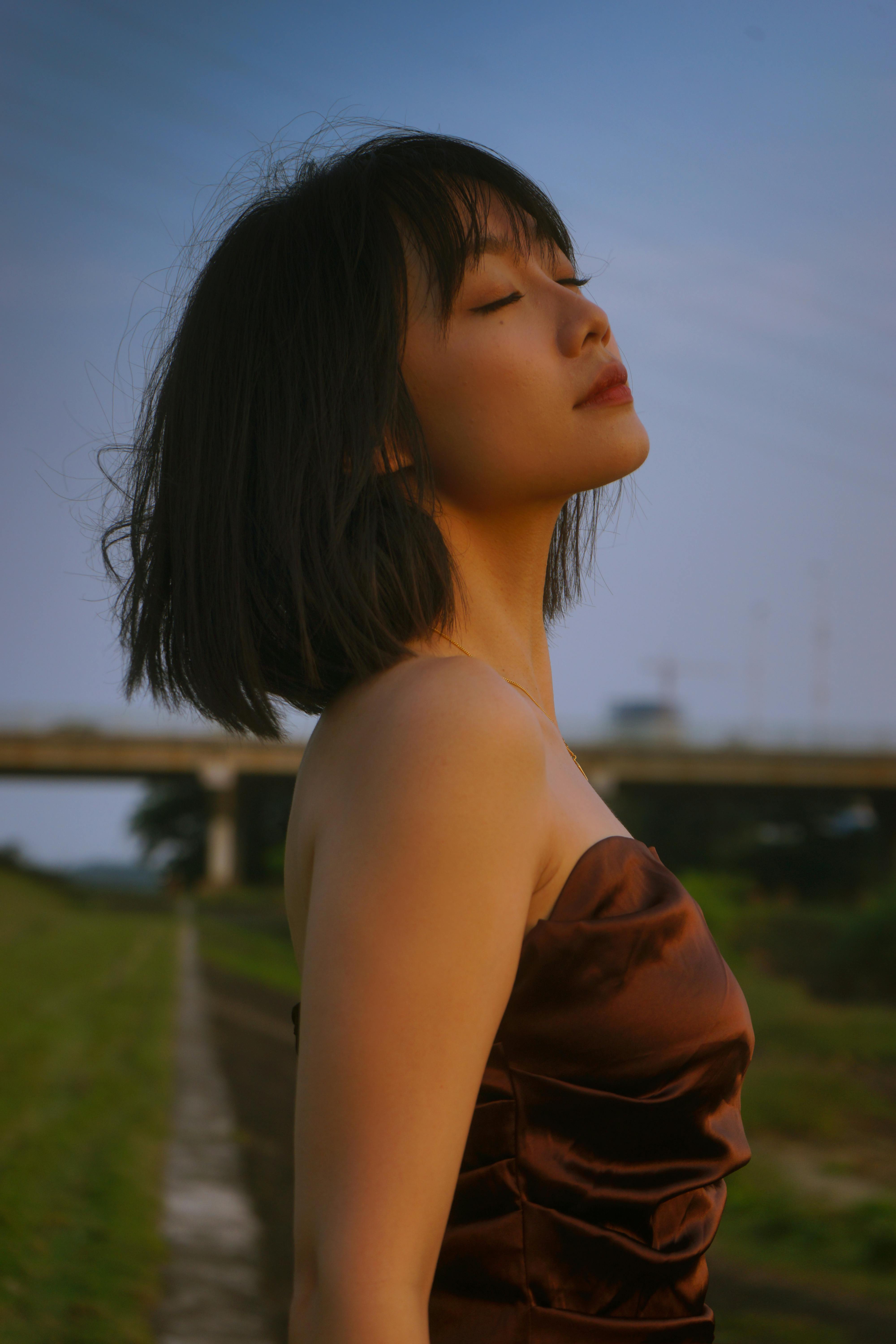 Young woman in a meadow, eyes closed, appreciating tranquility.