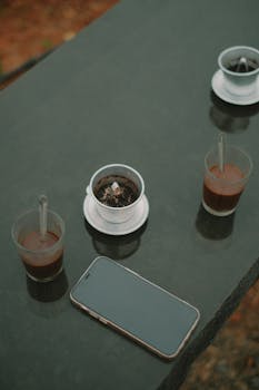 A modern setting with coffee cups and a smartphone on a stone table outdoors.