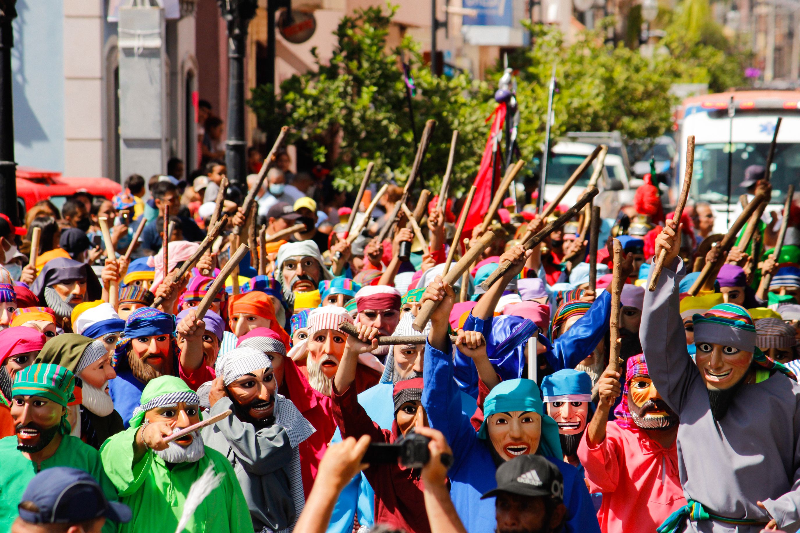Colorful masked parade participants with sticks in Mexican festival.