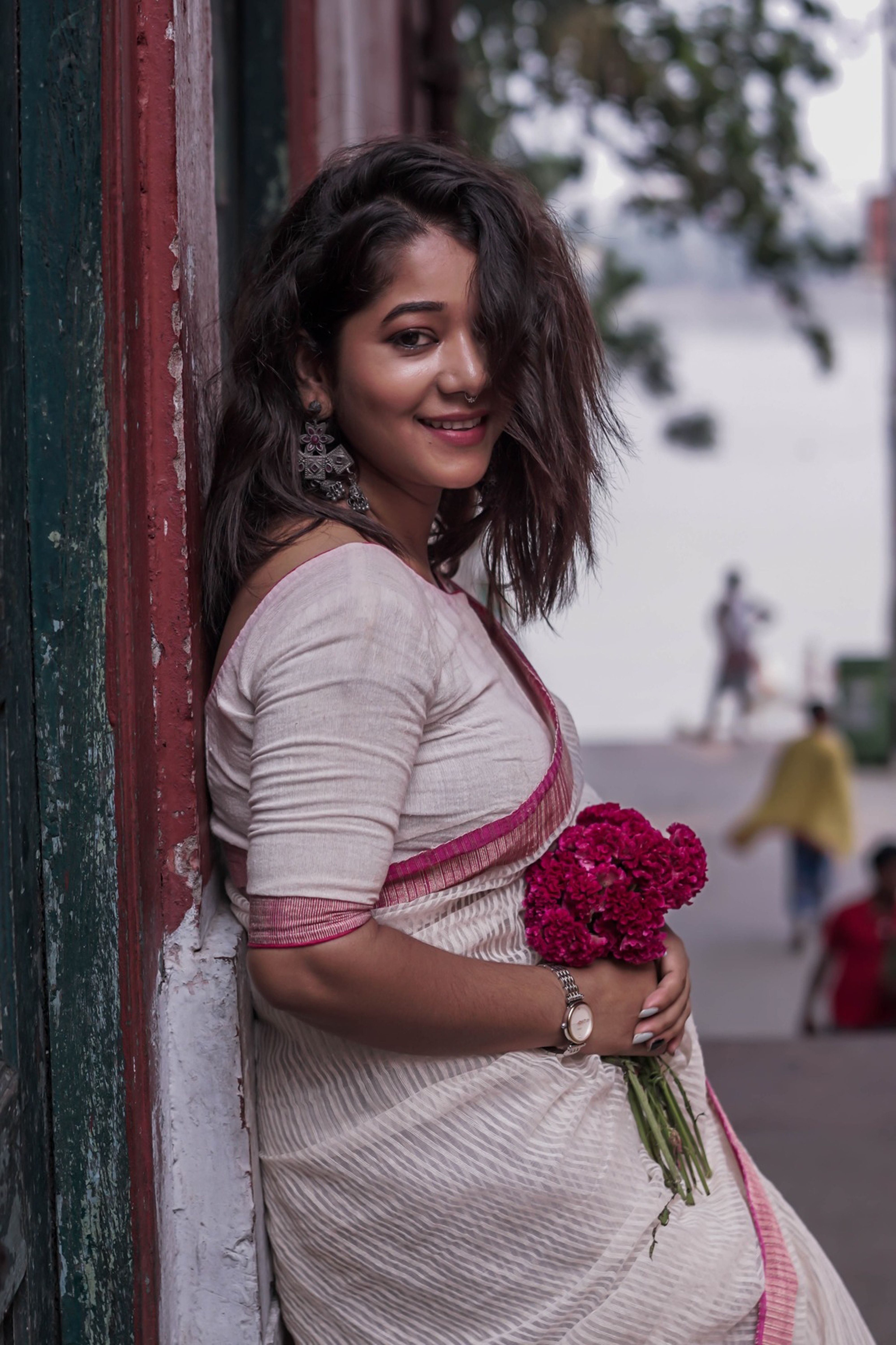 Charming portrait of a woman in traditional attire holding flowers and smiling outdoors.