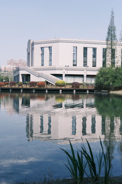 Free A modern architectural building reflecting in a serene pond surrounded by greenery in an urban park. Stock Photo