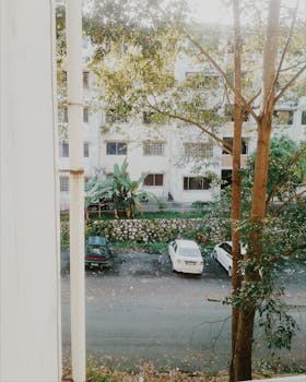 白天，现代化的公寓楼前停放着汽车，周围绿树成荫