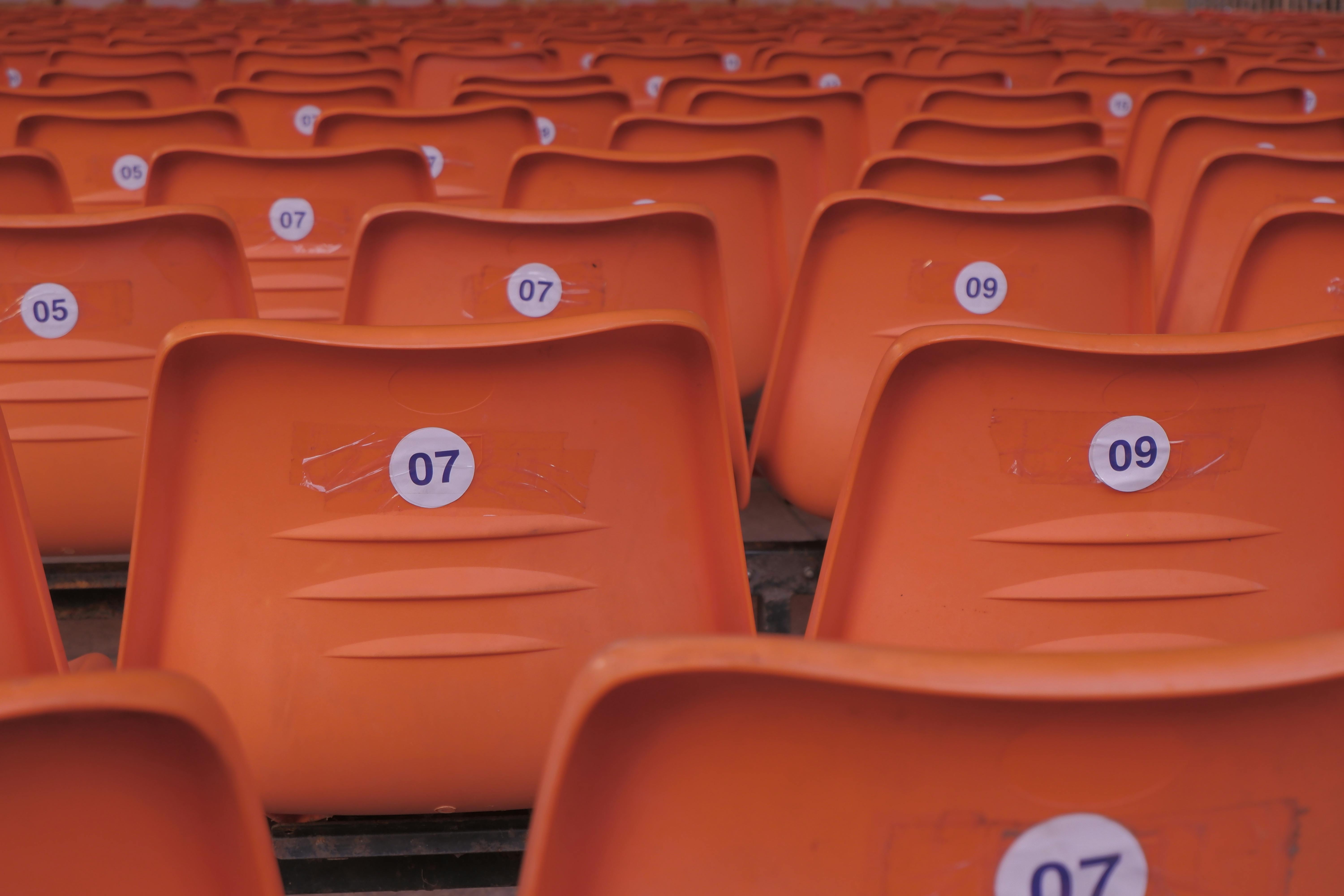 Rows of empty orange plastic stadium seats with visible numbered labels