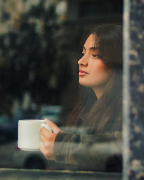 Free A young woman gazing thoughtfully out a café window while holding a mug of coffee in Tetouan, Morocco. Stock Photo