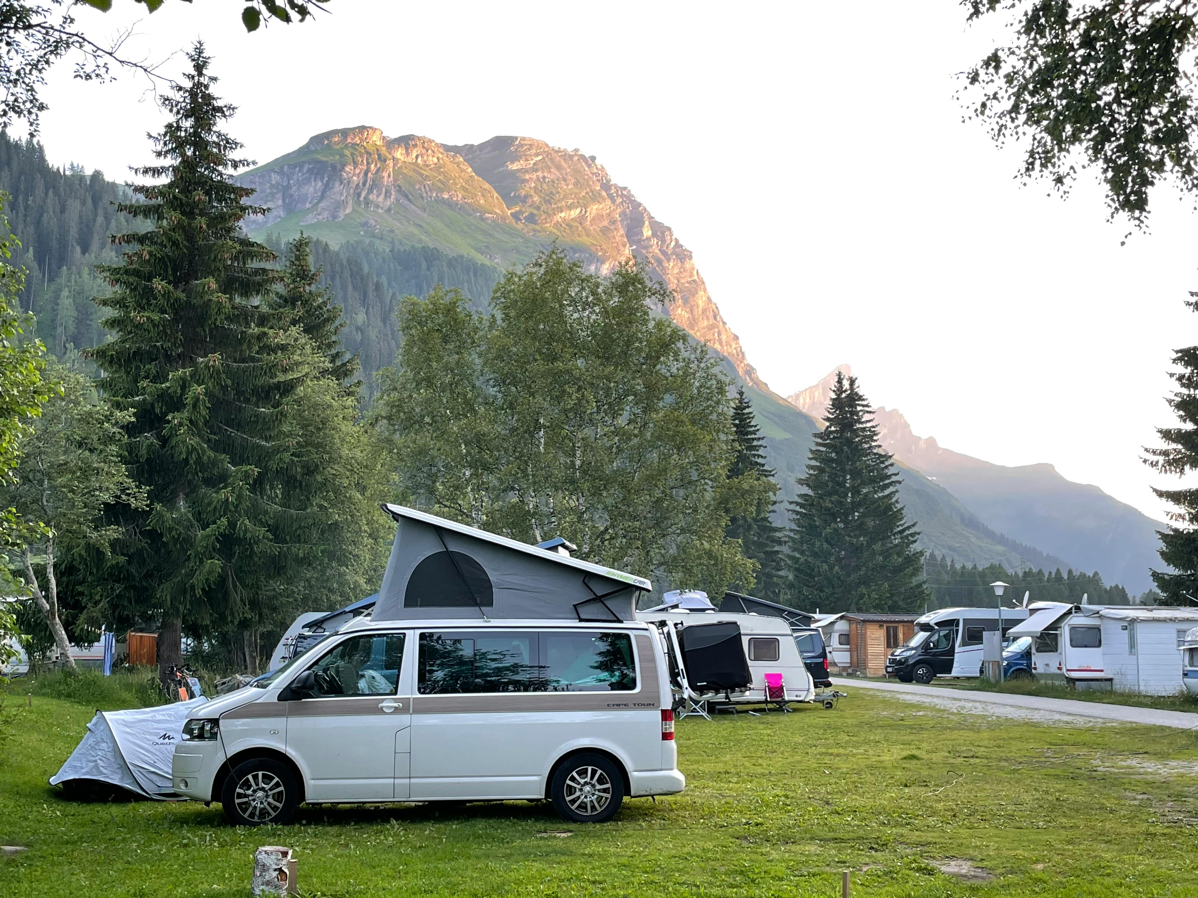 A serene camping site in Rheinwald, Switzerland with scenic mountains and parked camper vans.