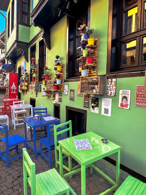 Free Vibrant outdoor cafe with colorful tables, chairs, and pot plants on a lively green building facade. Stock Photo