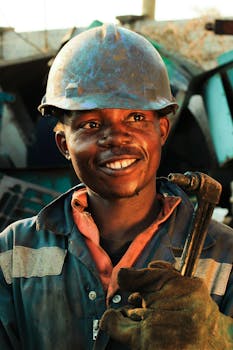 Close-up of a smiling construction worker in protective gear holding a tool at a worksite.