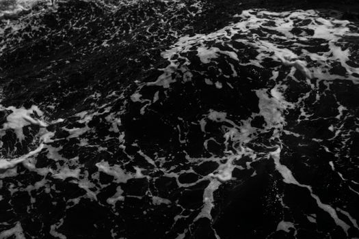A high-contrast black and white image capturing intense ocean waves with swirling foam.