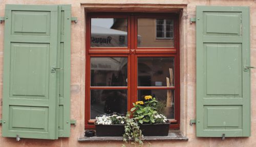Free Window with green shutters and colorful flowers in the flower box outside a vintage building. Stock Photo