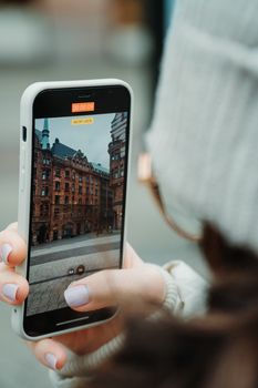 Woman captures Malmö street view with smartphone, focusing on historic architecture.