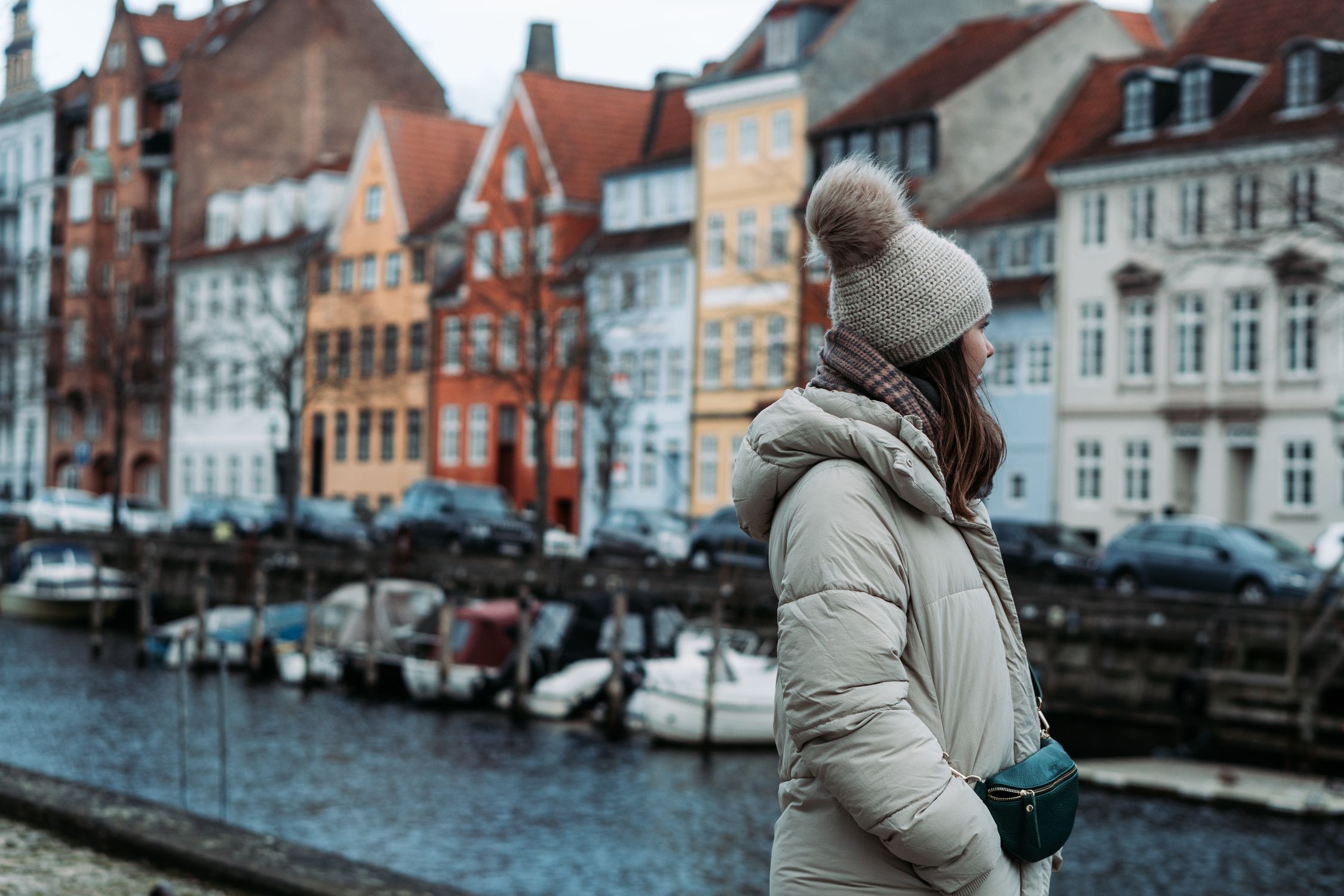 Woman in winter attire by colorful canal buildings in Copenhagen, capturing urban style.