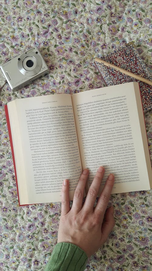 A person's hand holding a book and a camera