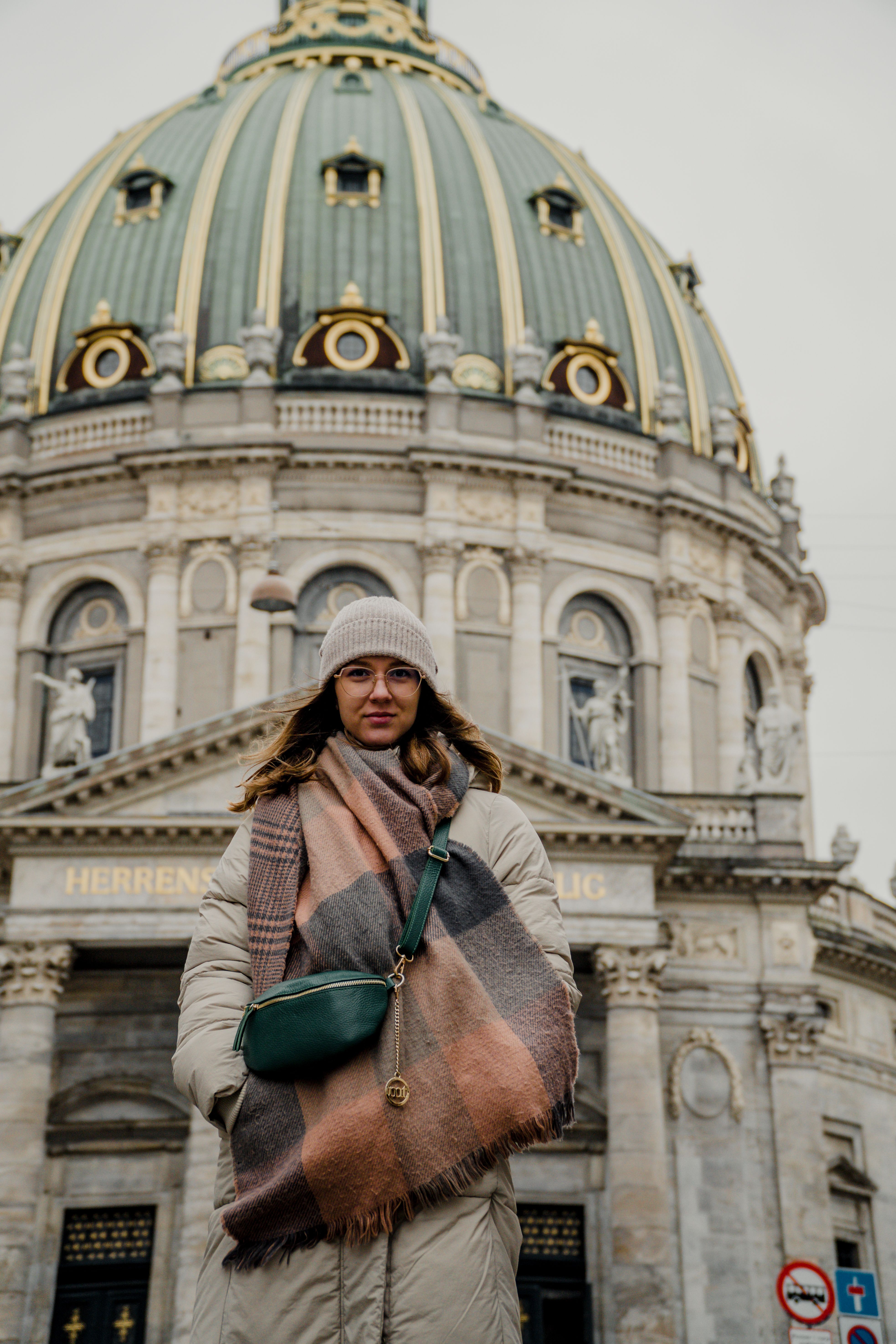 Woman standing in front of Frederik's Church in Copenhagen, wearing a cozy jacket and headgear.