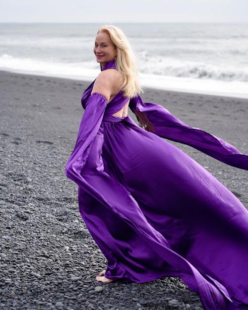 A woman in a purple dress is standing on the beach