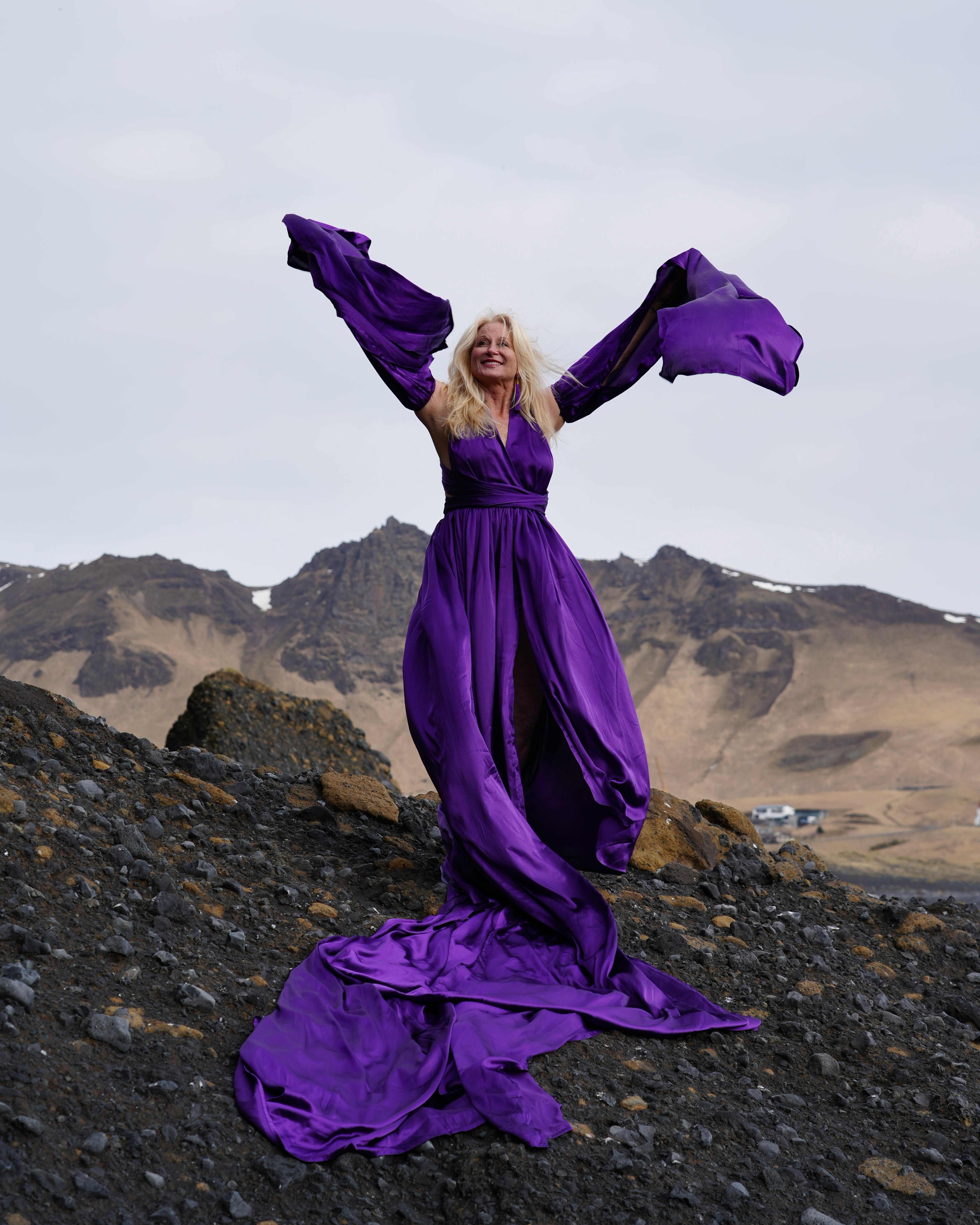 A woman poses gracefully in a flowing purple dress amidst Iceland's rugged landscape.