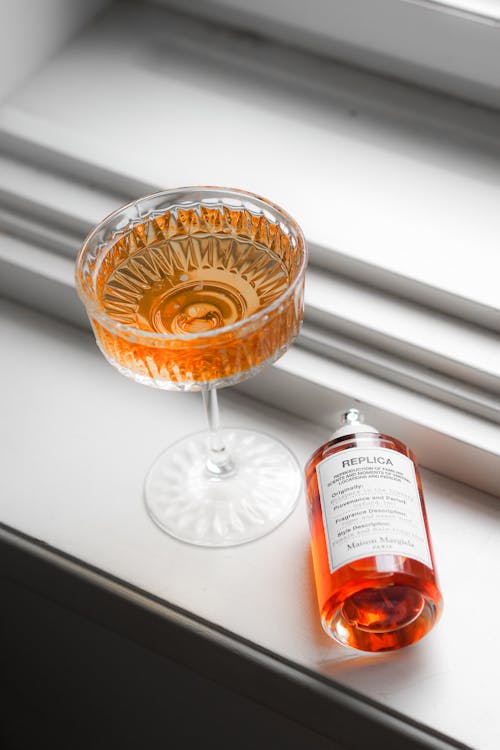 Orange Liquid in Wineglass by Perfume Bottle on Windowsill