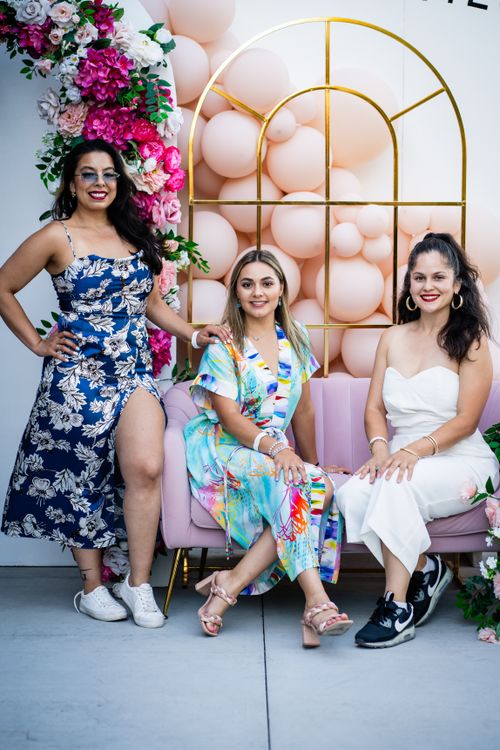 Free Three fashionable women in colorful dresses pose with smiles at a stylish celebration. Stock Photo