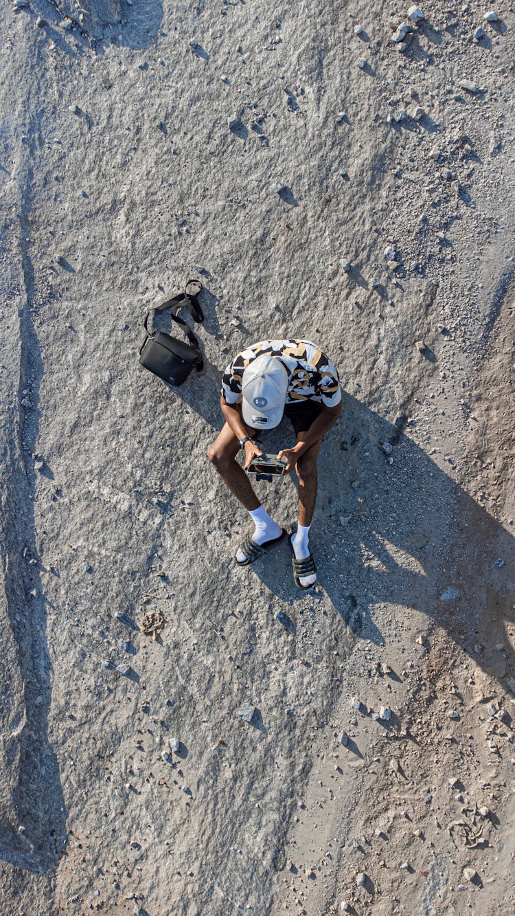 A Person Sitting On A Rocky Road Holding Drone Remote