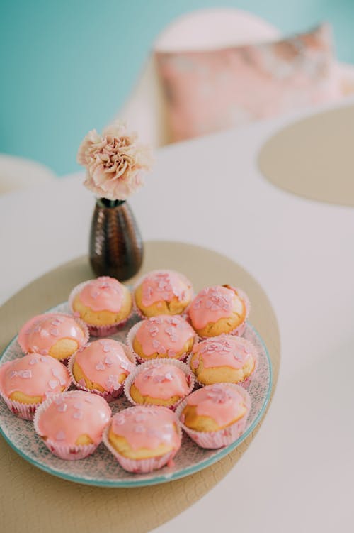 A plate of cupcakes on a table with a vase