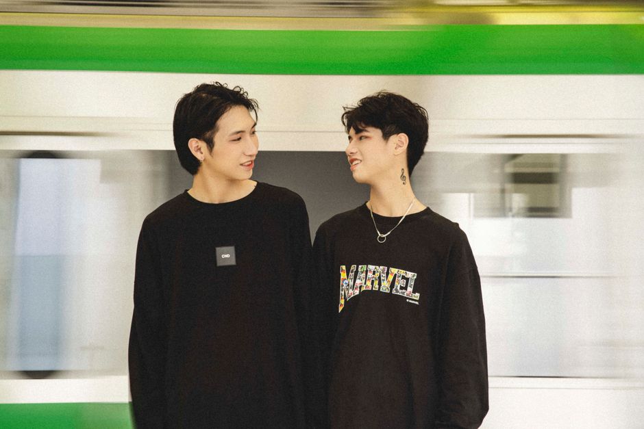 黒いプルオーバーを着た2人のアジア人男性が、都市の鉄道駅で現代のファッションと都市生活を体現しています。
