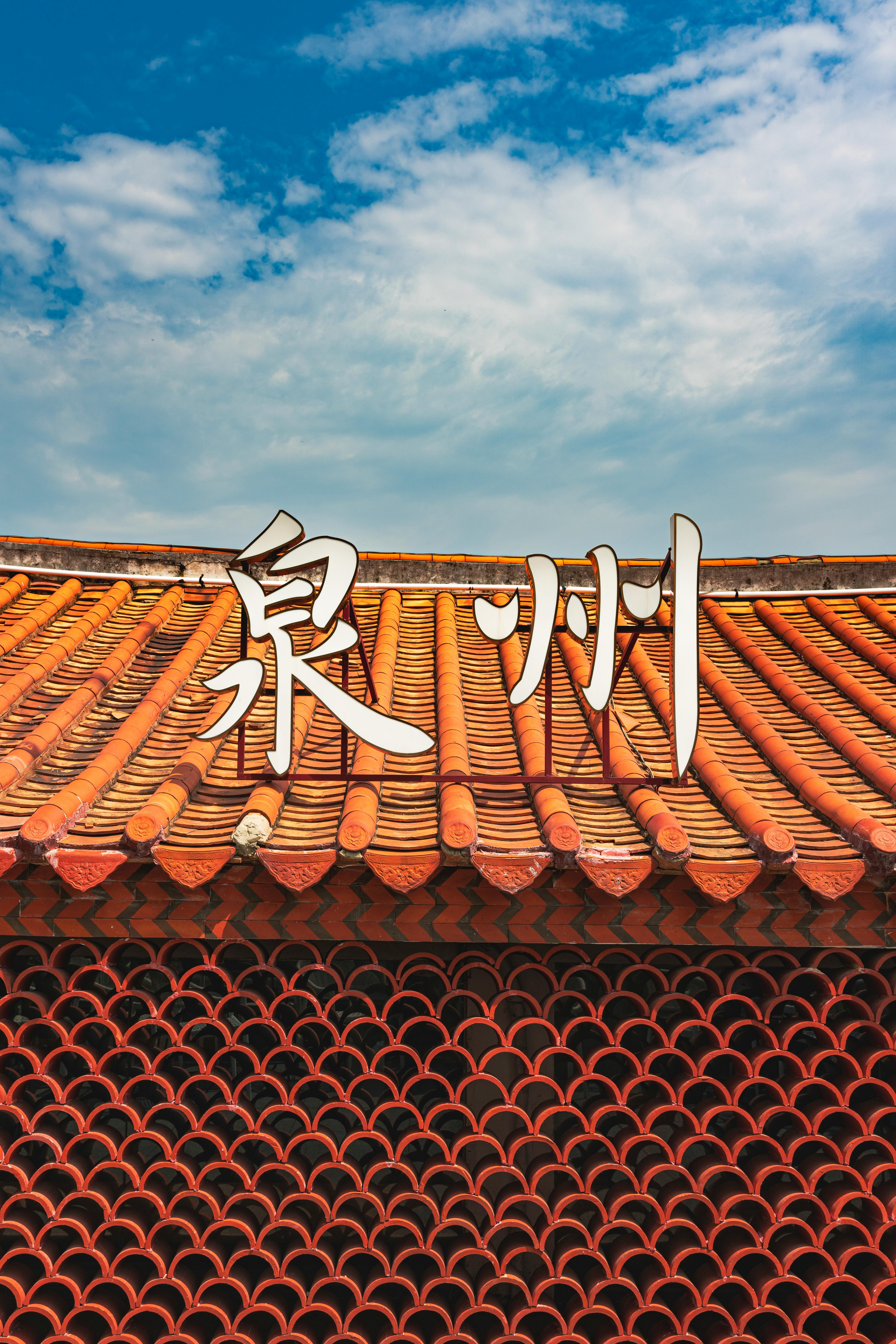Close-up of a Chinese building roof with traditional tiles and calligraphy against a blue sky.