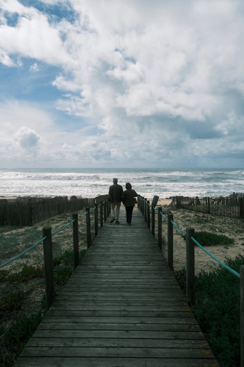 Two people walking on a wooden walkway to the beach