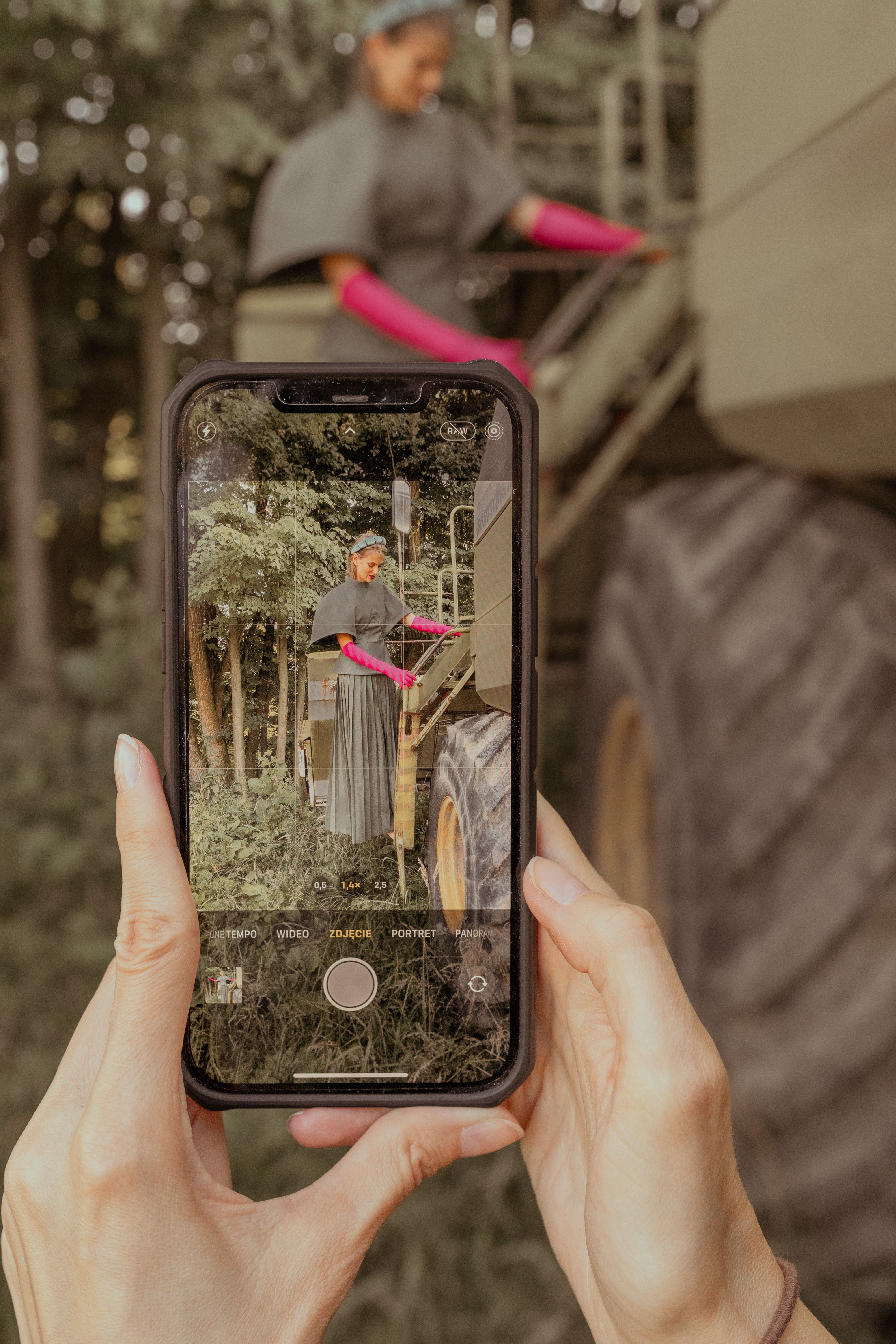 Close-up of a woman photographing a worker on machinery with a smartphone.