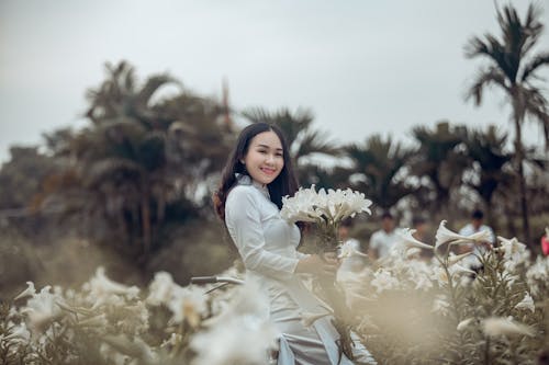 Woman in White Dress Standing and Holding White Petaled Flower and Smiling