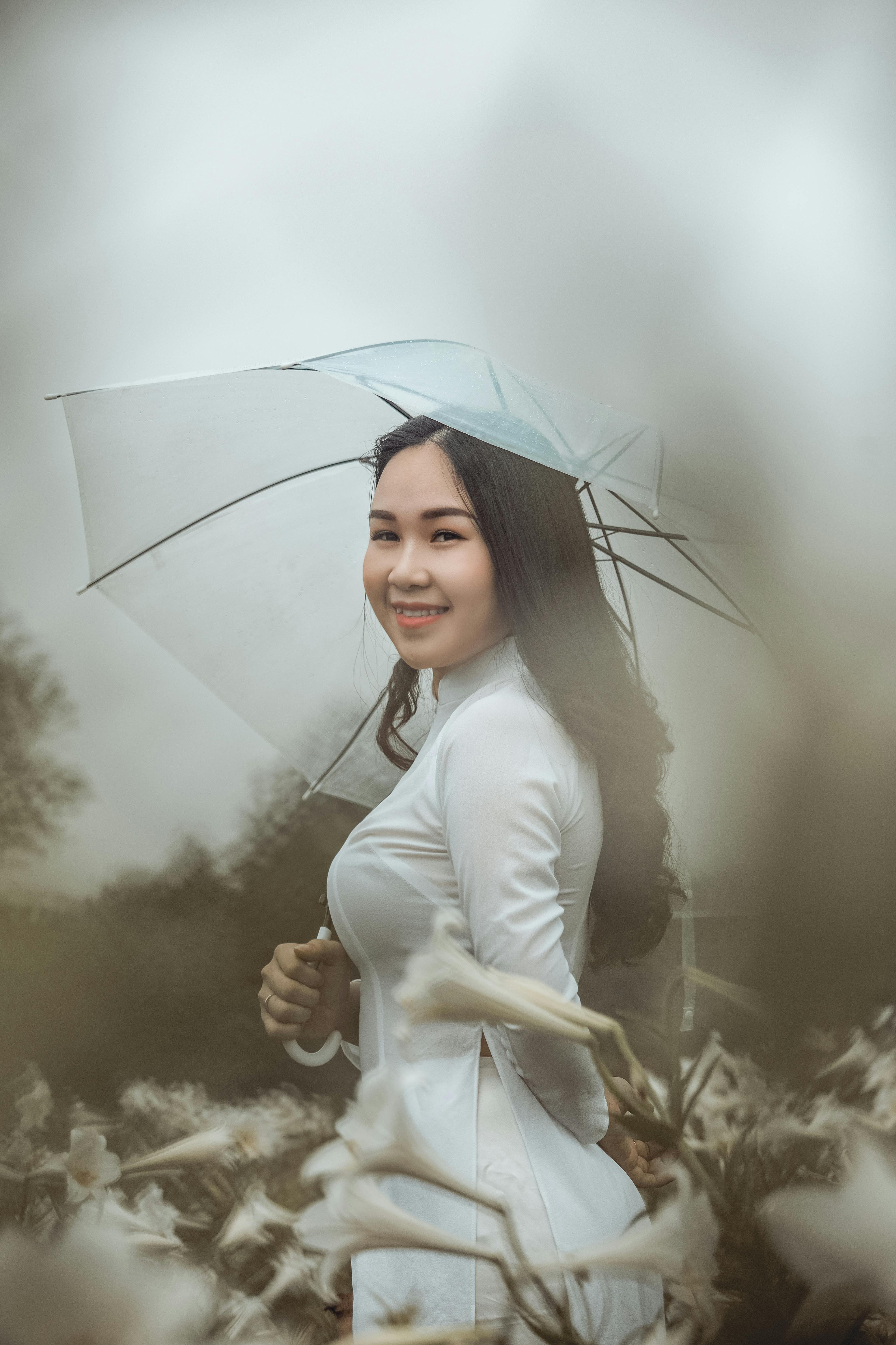 smiling woman wearing white long sleeved dress holding white umbrella