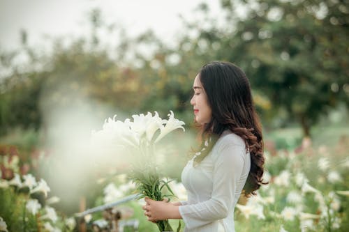 Woman in White Long-sleeved Dress Holding White Flowers on Selective Focus Photography