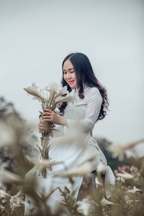 Free Serene moment of a woman in a white dress holding a flower bouquet outdoors in a field. Stock Photo