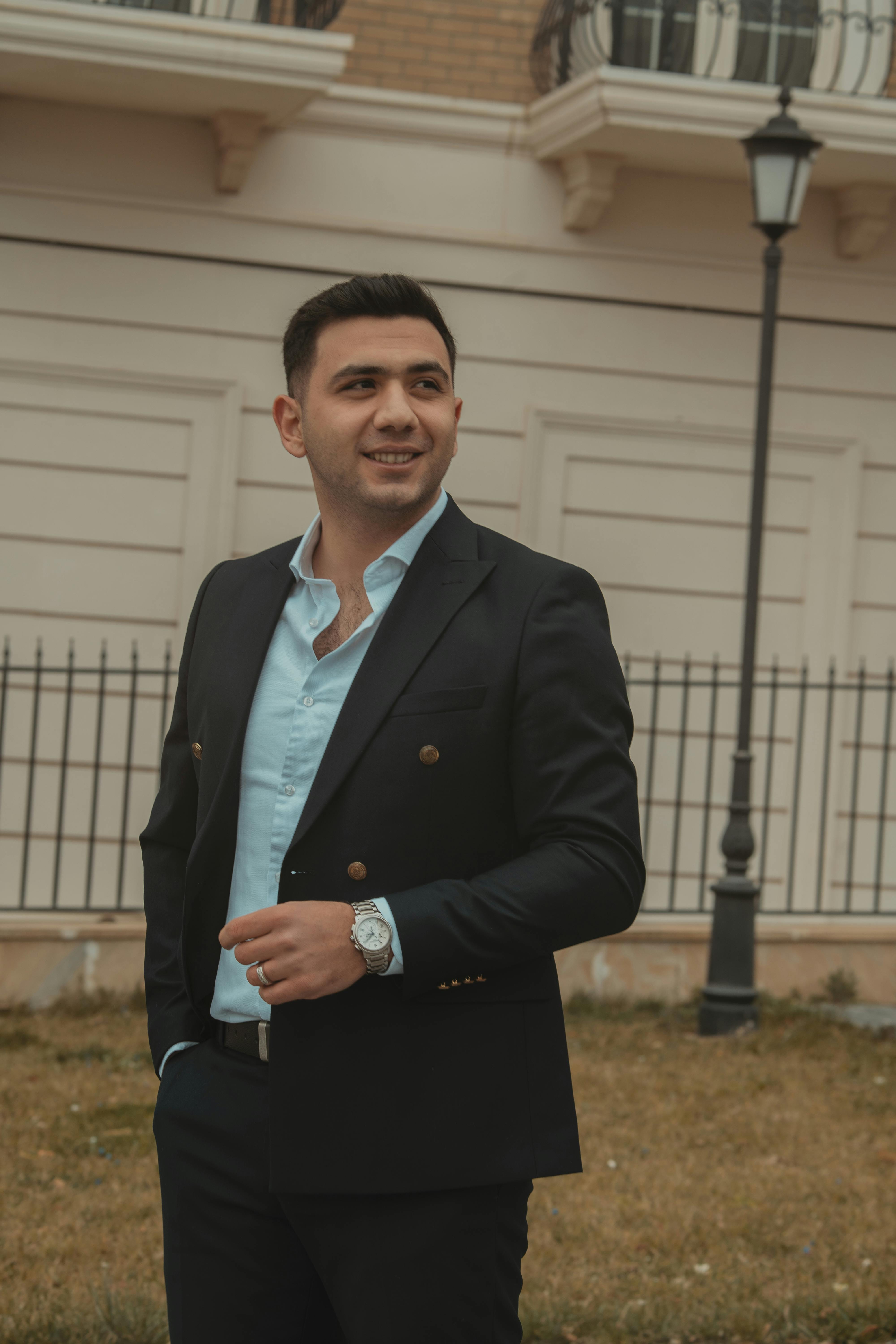 Stylish young adult man in a suit, smiling confidently in an urban outdoor setting.