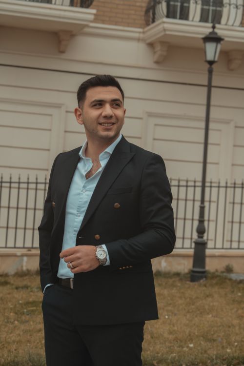 Free Stylish young adult man in a suit, smiling confidently in an urban outdoor setting. Stock Photo